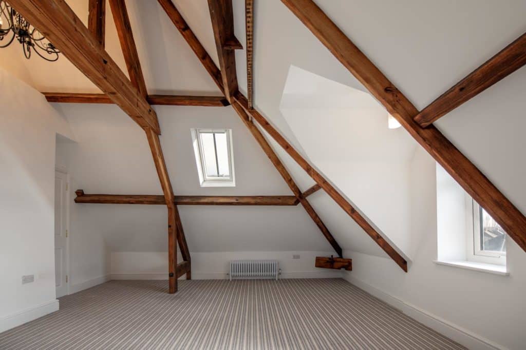 spacious bedroom painted white, with historic beams 