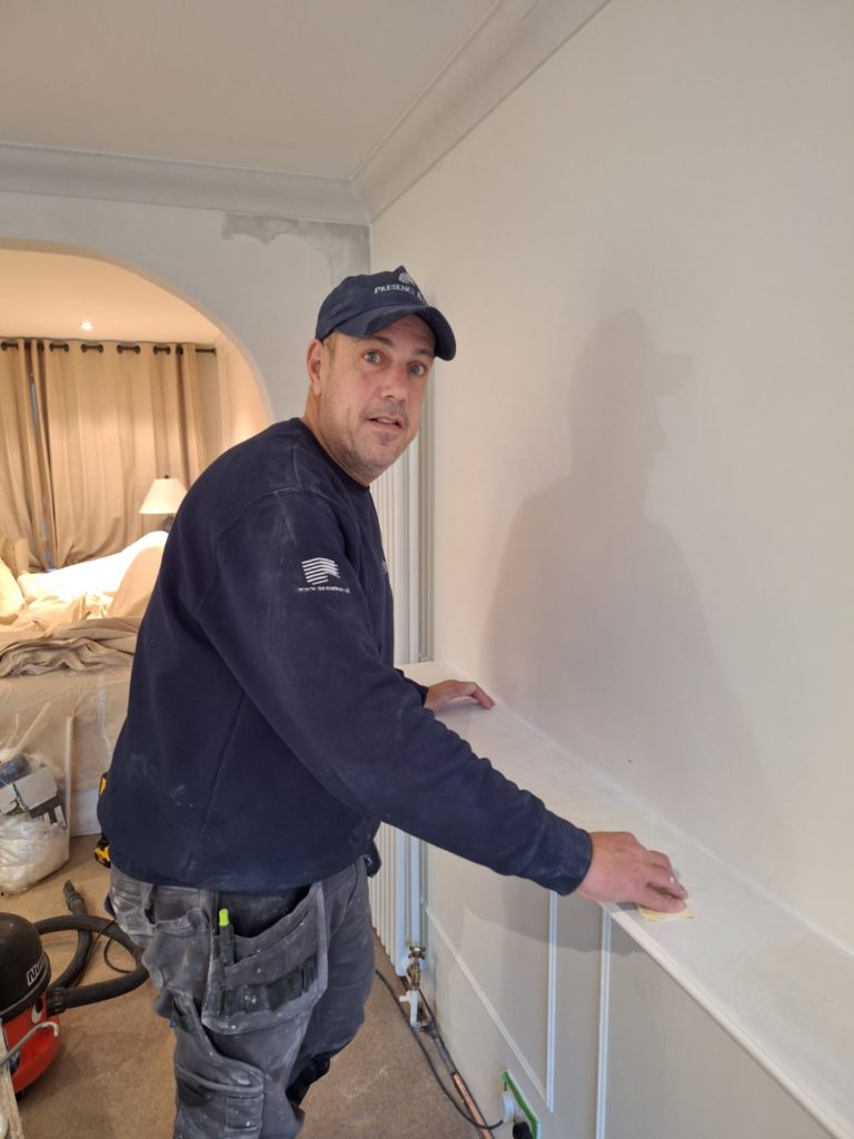 Rob Laing pictured in beige toned room where he is currently working. Wearing Presence & Co. navy branded uniform