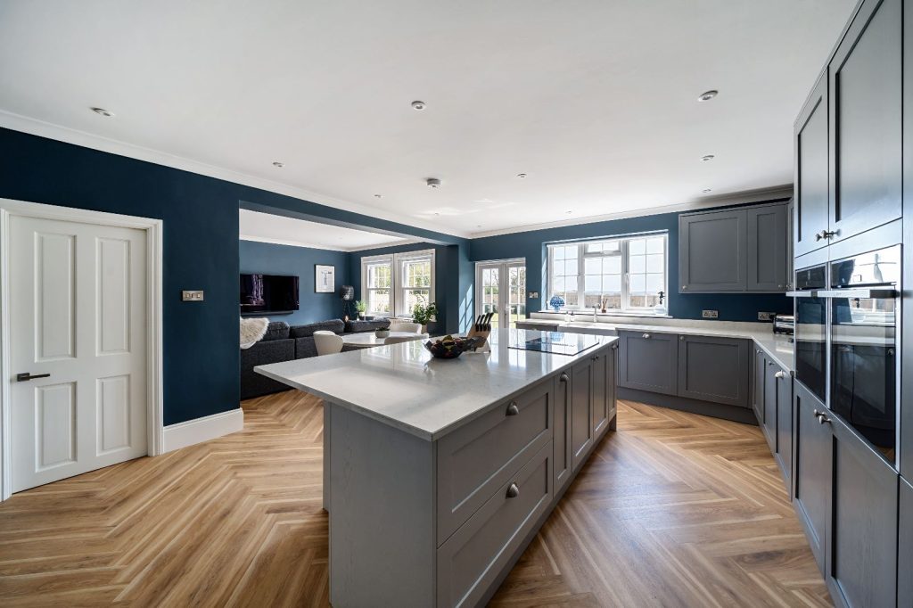 open plan kitchen with woodnen island, wooden floor and gorgeous open plan lighting. dark blue walls, grey counter tops 