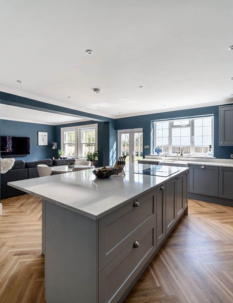 open plan kitchen with woodnen island, wooden floor and gorgeous open plan lighting. dark blue walls, grey counter tops