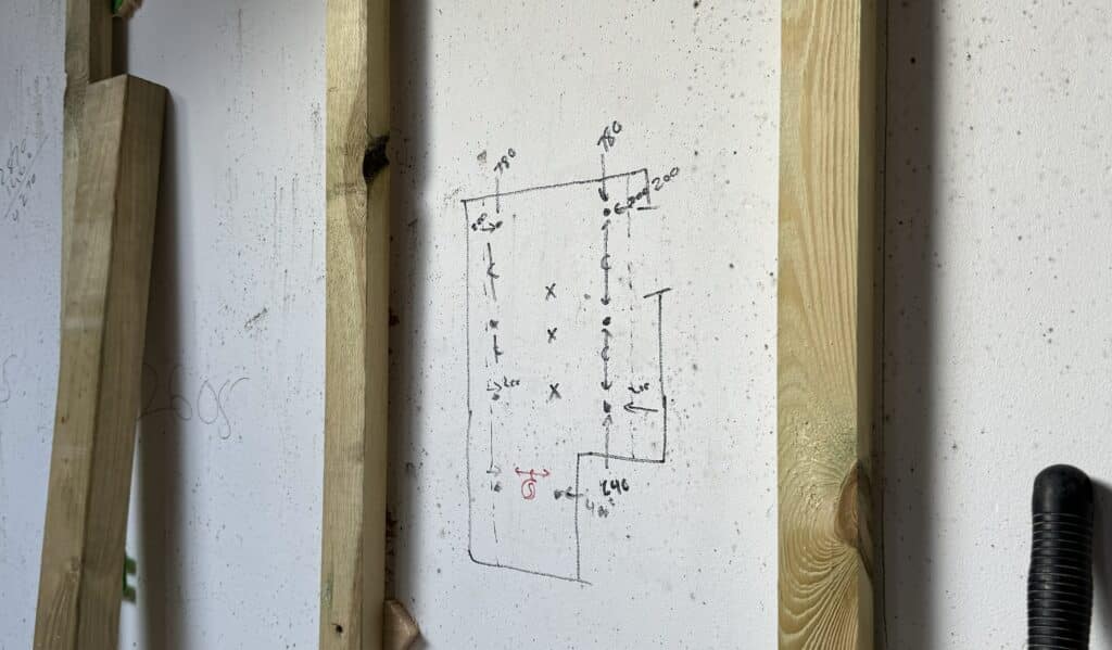 A picture of a wall with wooden boarding, drawn on the wall is a first fix plan on wall before plastering and installation.
