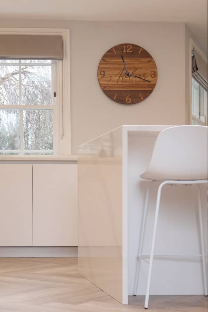 freshly painted kitchen in white, with brown wall clock and a table and stool featuring.