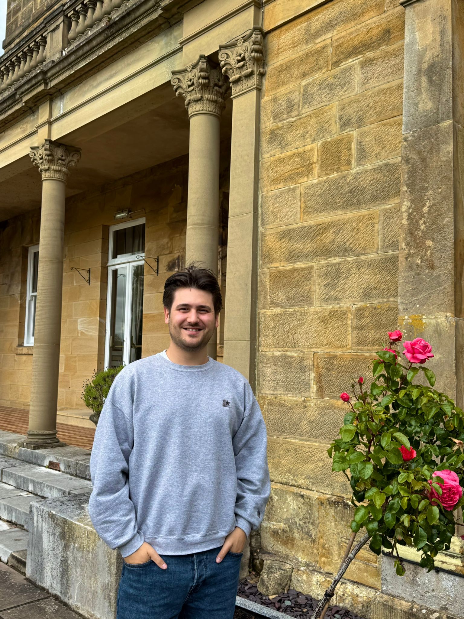 Sam, Administrator, stoof outside a yellow brick building with pink roses in the background