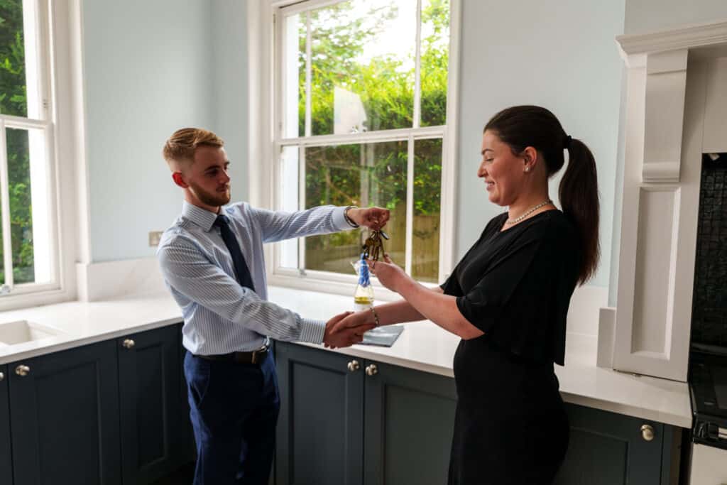 estate agent closing a deal on a property, sshaking hands and handing over the keys. a bottle of celebratory chapagne is seen in the back